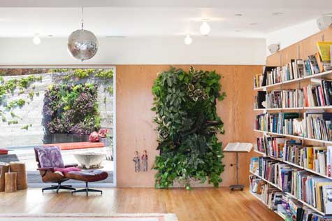 Woolly Pockets Photo of a living room with a window revealing a garden on the left, a vertical hanging garden in the centre and a bookcase to the right.