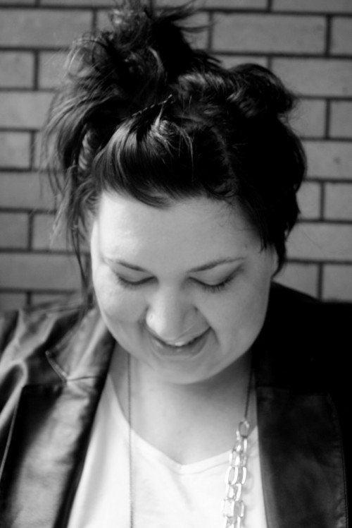 moi A black and white, head and shoulders, photo of me. I'm looking down, my hair is up, and I'm wearing a leather-look jacket with a white tshirt and a big chain necklace.