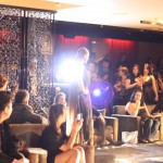 Alexi Freeman Model walking down a runway amongst a crowd of people with camera flashes popping around her.