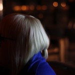 Hayley A blonde woman is on the left with out of focus ambient light to her right.
