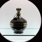 Chambord, the hero! A bottle of Chambor (a dark purple liqeur in a gold accented fancy bottle) sits on a shelf with a white background.