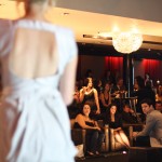 Our lovely host (whose name escapes me, embarrassingly) A woman in a light coloured dress with a window-hole back has her back to us, to the right is the crowd (in focus).
