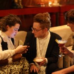 Greta, Nathan and Clea A woman on her phone, a man holding a martini and another woman holding a martini chat.