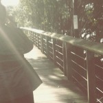 Photo of Natalie's silhouette, she's walking away from the camera along a wooden walkway into a solar flare.