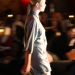 above. Side profile of a model walking in a grey romper-style design - with bracelet length sleeves and short shorts.