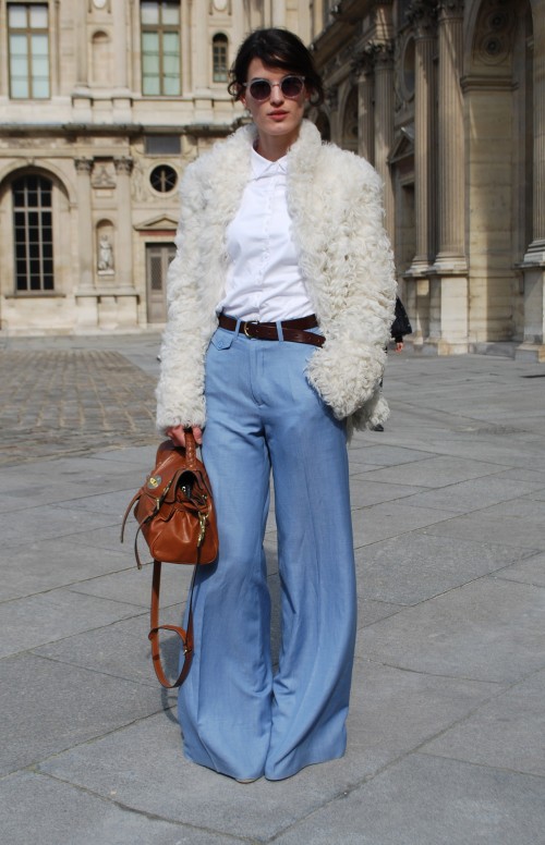 From Stylesightings A young slim pale skinned woman wearing a white buttoned up shirt with blue flared jeans and a brown belt. Over the outfit she wears a white fur (looks faux!) jacket, and she carries a tan leather bag.