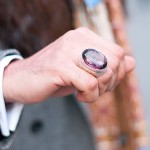 A close up of a man's hand wearing a spectacularly huge purply coloured gem ring.