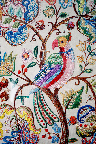 Bird embroidery Detail photo of an embroidered piece of fabric with a brightly coloured bird sitting in a tree with paisley-like symbols as the foliage.