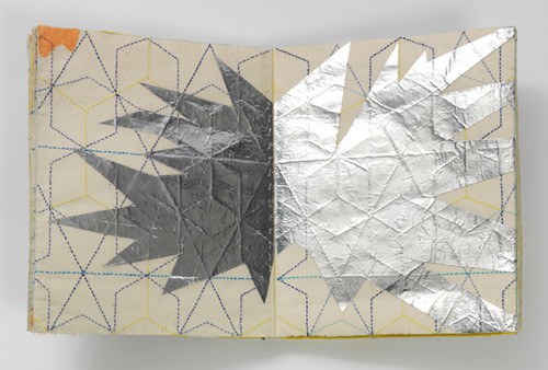 An open book, the spread embroidered with a geometrical pattern and an explosion-like graphic has been laid over the top, perhaps in silver leaf?