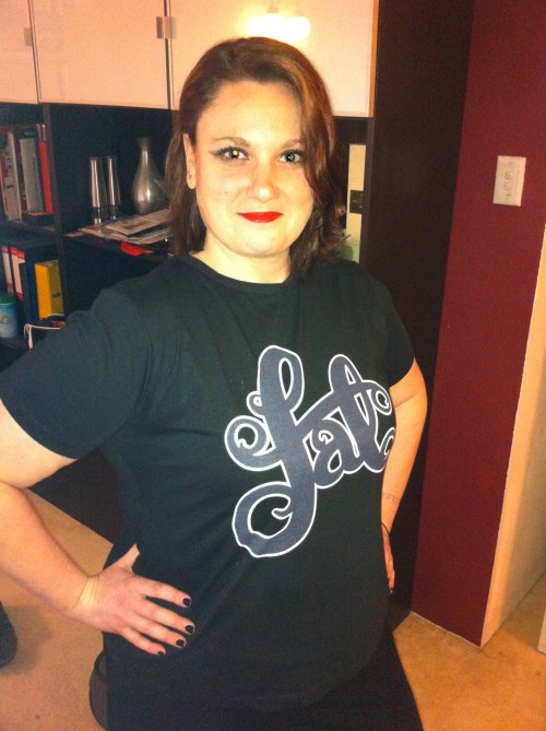 A fat white woman wearing a black t-shirt that says "fat" in curvy typography.