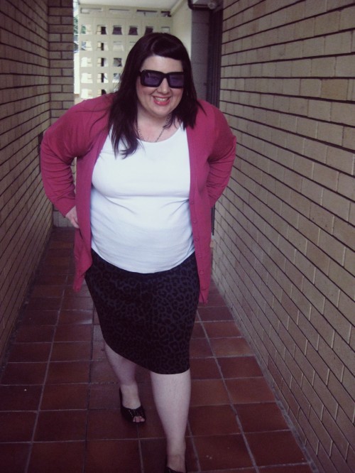 Outfit photo of me wearing a white tank top with a black/ grey animal print pencil skirt and a pink cardigan. I'm walking towards the camera with my hands on my hips, smiling.
