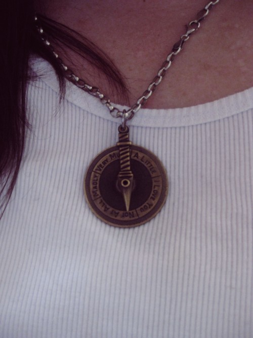Macro photo of a bronze pendent that consists of a disc attached in the centre to an arm. The markings around the disc read "I love you - Not at all - Madly - Very much - A little"