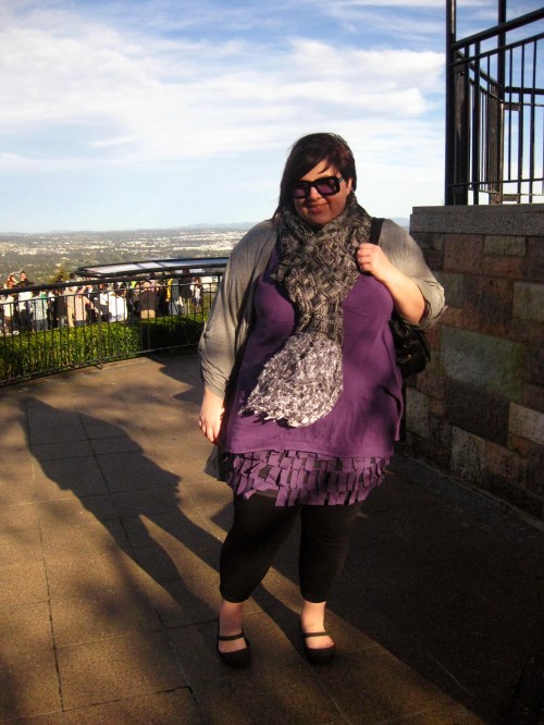 Photo of me on top of Mt Coot-tha. I'm wearing a long purple top over a fringey purple skirt, a grey long cardigan and scarf with black tights and shoes.