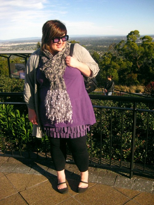 Photo of me on top of Mt Coot-tha. I'm wearing a long purple top over a fringey purple skirt, a grey long cardigan and scarf with black tights and shoes.