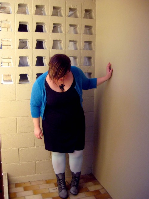 Photo of me posing for an outfit photo, wearing a black dress, pale blue tights, grey boots and a blue sparkly cardigan.