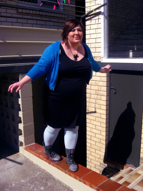 Photo of me balancing on a little ledge wearing a black dress, pale blue tights, grey boots and a blue sparkly cardigan.