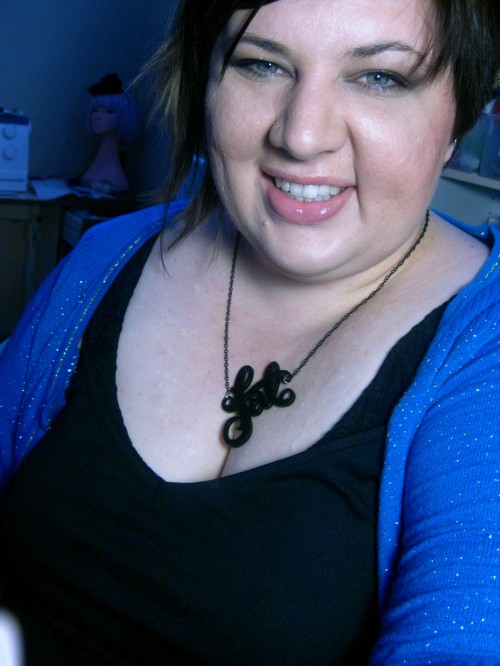 Head and shoulders shot of me wearing a necklace that says "fat" in curly lettering cut out of acrylic.