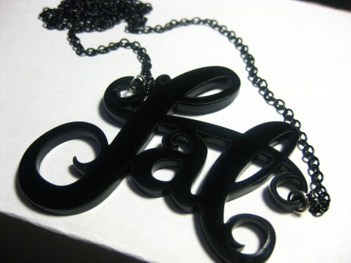 A necklace that says "fat" in curly lettering cut out of acrylic.