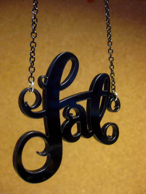 A necklace that says "fat" in curly lettering cut out of acrylic.