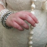 A photo of my right hand (with lots of bracelets) lightly clasping a very long cream bead necklace.