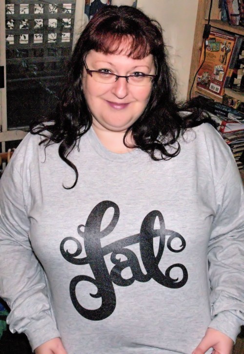 A fat white woman with long dark hair wearing a grey long sleeved t-shirt with "fat" written in curvy typography.