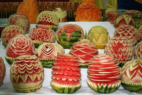 Photo of a bunch of gorgeous bright fucshia watermelons that have been carved in different, fancy ways. 