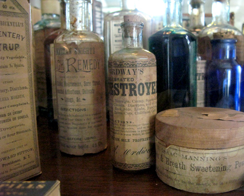 A photo of very old bottles and containers with aged labels that claim the contents to be remedies.