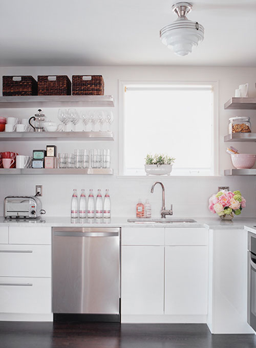 Photo of a crisp white kitchen with lots of light, floating shelves holding neatly arranged baskets, glasses and other things.