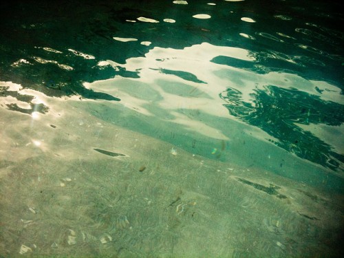 Photo of water in a pool, the light is dancing on the gently rippled surface and the water looks a deep greeny/ blue.