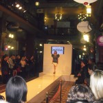 A model walks down the catwalk wearing a black and white patterned dress with huge ruffled shoulders.