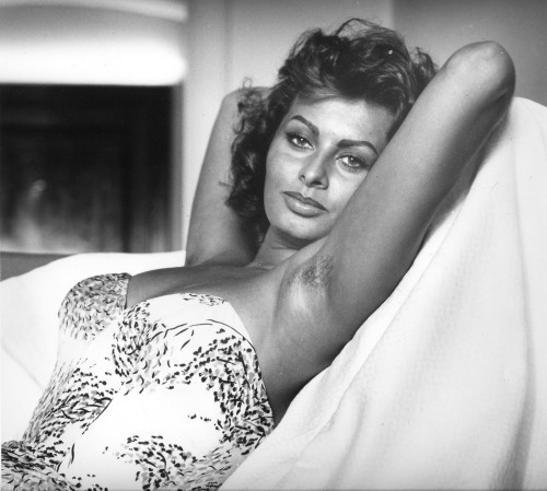 A black and white photograph of Sophia Loren reclining in a strapless top, her arms behind her head. Her armpits are scattered with fine hair.