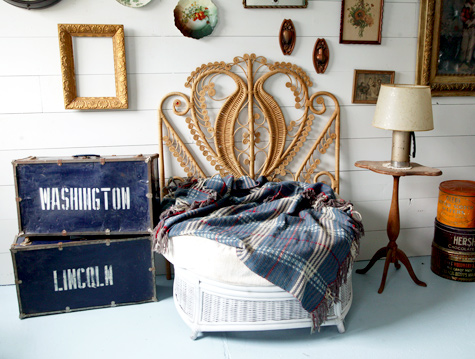 Photo of a chair with a big ornate backing made of cane, there's also a bunch of old pictures and frames on the wall. 