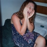 Photo of me as a teenage girl with pale skin and sunburnt arms jokingly screaming in pain. A spider sticker has been stuck in my lap.