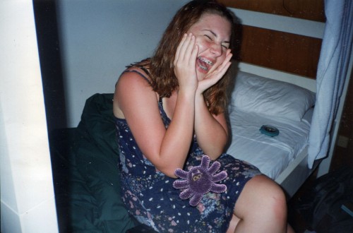 Photo of me as a teenage girl with pale skin and sunburnt arms jokingly screaming in pain. A spider sticker has been stuck in my lap.