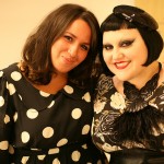 Photo of Sakina wearing the polka dot dress with Beth Ditto, who wears the floral dres with a feathered statement necklace and a small sequinned beret like headpiece.
