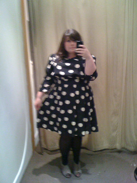 Blurry change room photo of a young white chubby woman wearing the polka dot dress.