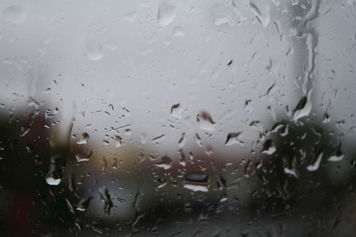 Macro photo of rain droplets on a window with blurry dark shapes outside.