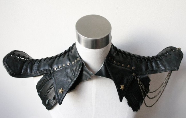 Photo of a shoulder piece sitting on a white dress form. The piece is made of several bits of black leather with lacing, rivets and dangling chains.
