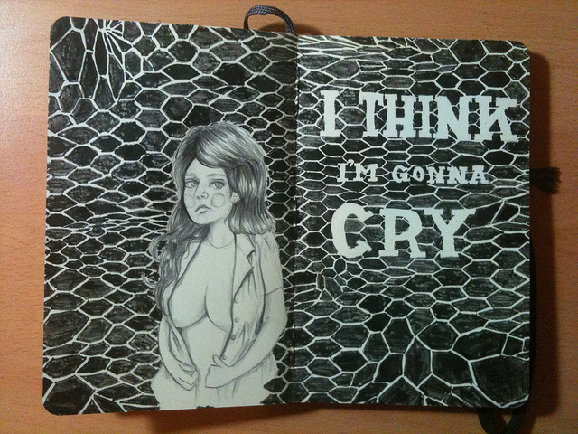 Photo of a drawing across two moleskine pages: a pencil drawing of a young woman with long hair, and an open shirt that just covers her breasts against an undulating fishnet pattern which has the words "I think I'm gonna cry" written in it.