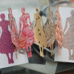Photo of one of those chain cut outs, with the cut outs being in the shape of a woman holding her skirt out. Each fold is a different print.