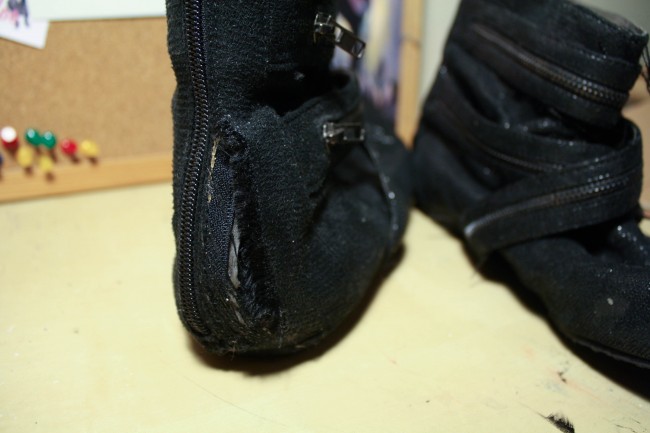 Detail shot of a rip in the back of a pair of black boots with zippers criss crossing around them.