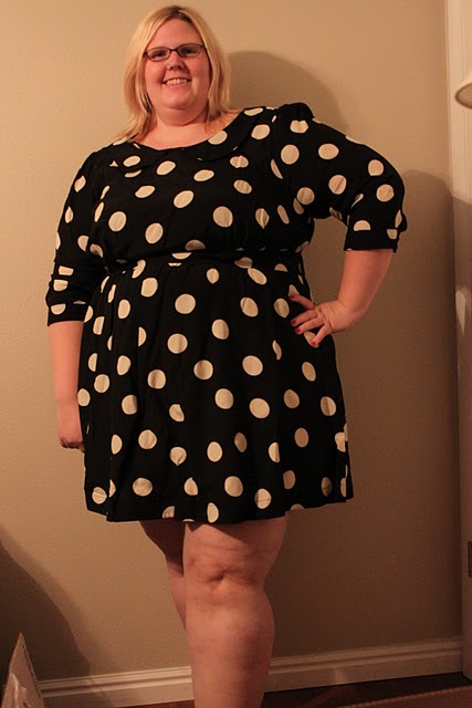 A photo of a fat pale skinned woman with blonde hair and glasses wearing the polka dot dress and smiling.