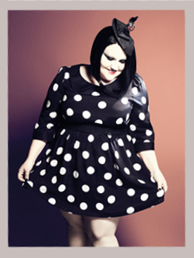 Photo of Beth Ditto wearing a black dress with large white polka dots. The skirt is short and has a bit of fullness, the sleeves are elbow length and there is a little Peter Pan collar.