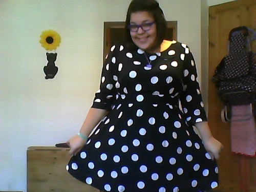 A young olive skinned woman with short brown hair and glasses wearing the polka dot dress.
