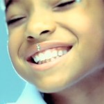 Still from Willow Smith's Whip My Hair Video: close up on Willow smiling. She's got some little rhinestones stuck down the middle of her top lip.