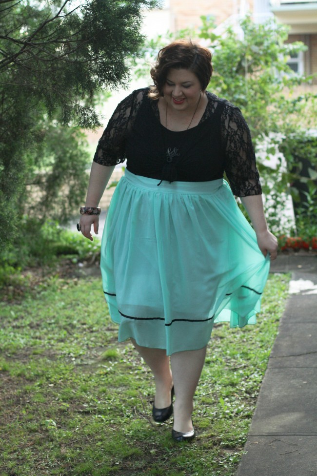 Outfit photo of me in a dress with a black top and full pale blue skirt, and a lace cardi tied under my boobs. My hair is curled and I'm wearing black shoes; I'm walking around a garden and you can see the outline of my hips as the light shines  through the skirt.