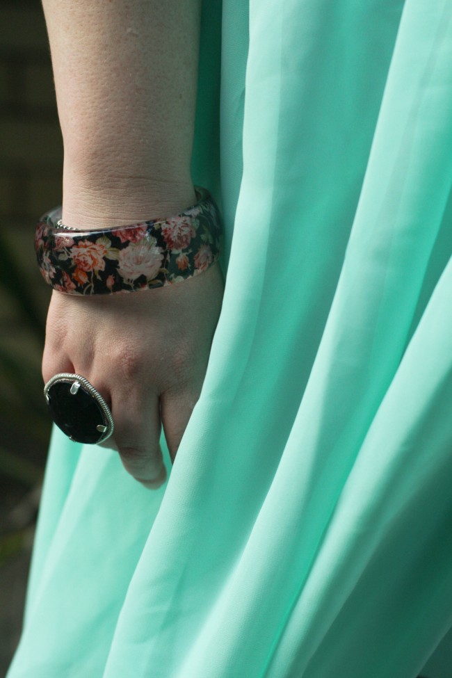 Close up photo of my hand next to my side, draped in pale blue chiffon, and I'm wearing a plastic bangle with a floral print, and a ring with a large flat dark stone.