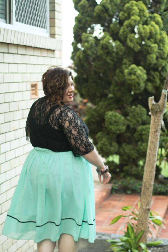Photo of me with my back facing the camera, and I'm looking over my shoulder. I'm wearing a black lace cardigan over a mint blue full skirt.