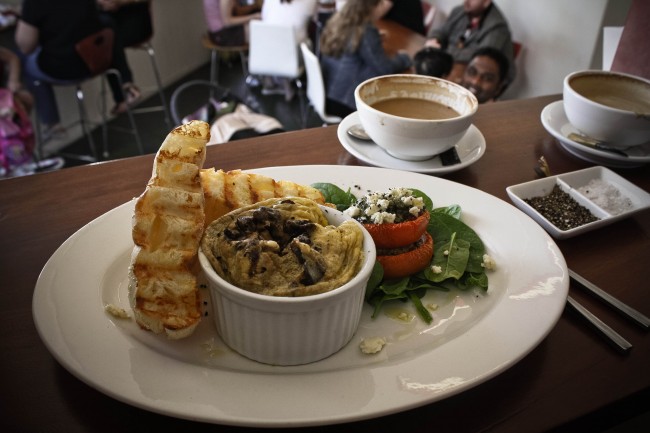 Photo of my breakfast, a mushroom and feta omelette in a souffle dish with three pieces of bread and some tomatoes with pesto sitting on spinach leaves.