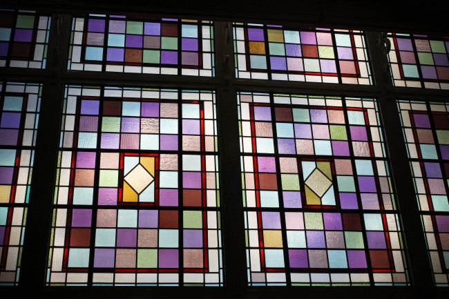 Photo of stained glass windows with mostly purple and lilac coloured glass squares with an odd oranged coloured square here and there.